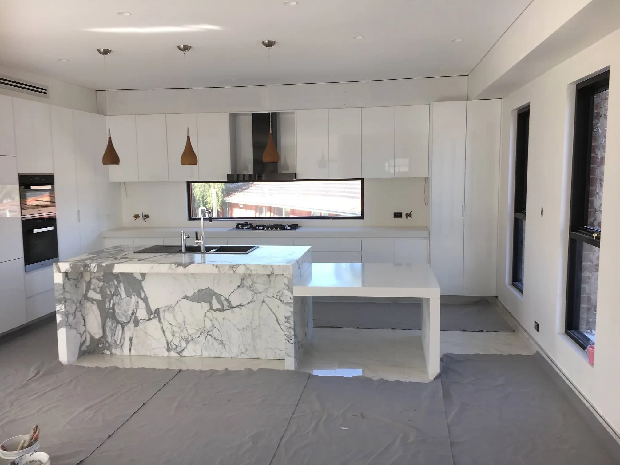 White kitchen with a marble-look waterfall island, pendant lights and a timber-lined bulkhead by H&R Kitchens