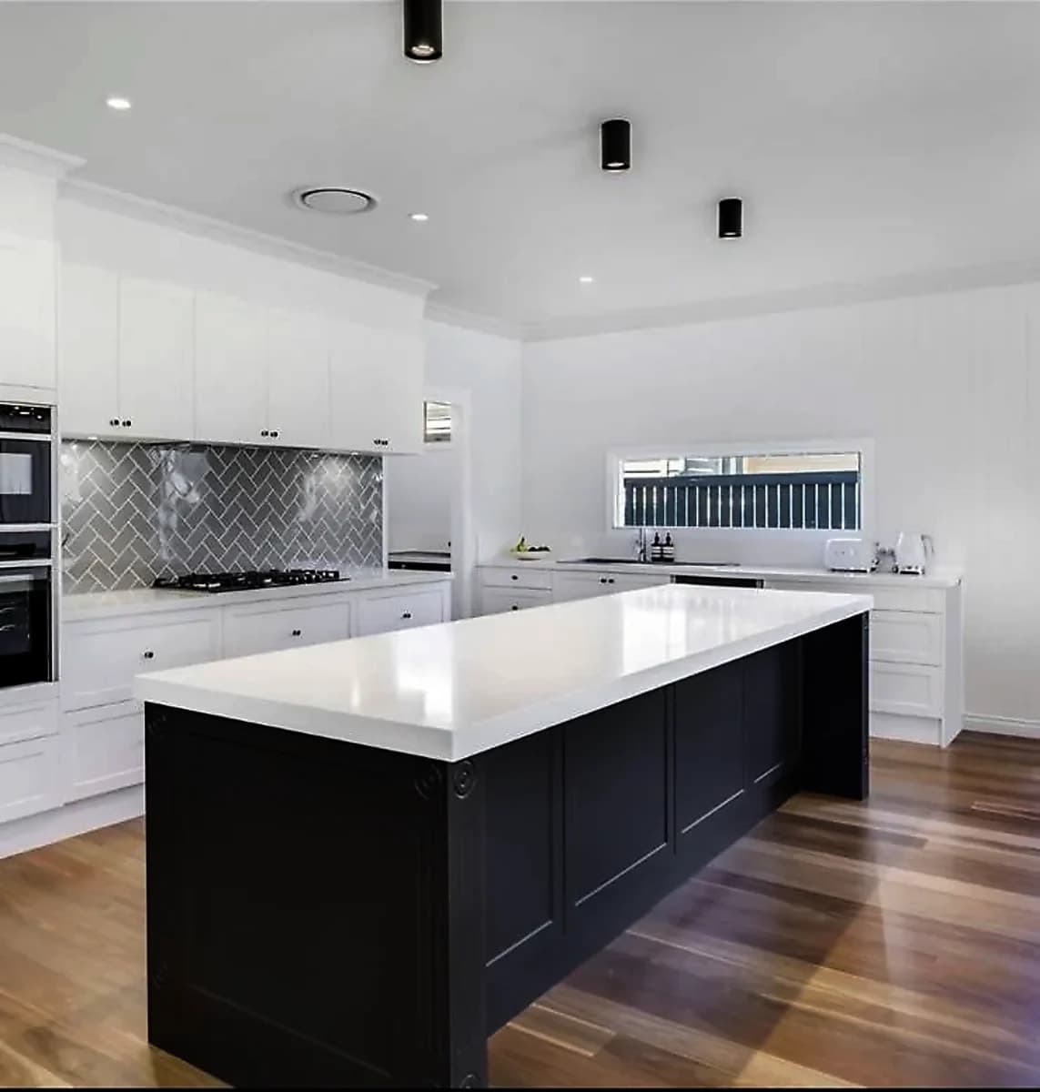 White kitchen with a black island, white benchtop and a herringbone tile splashback by H&R Kitchens