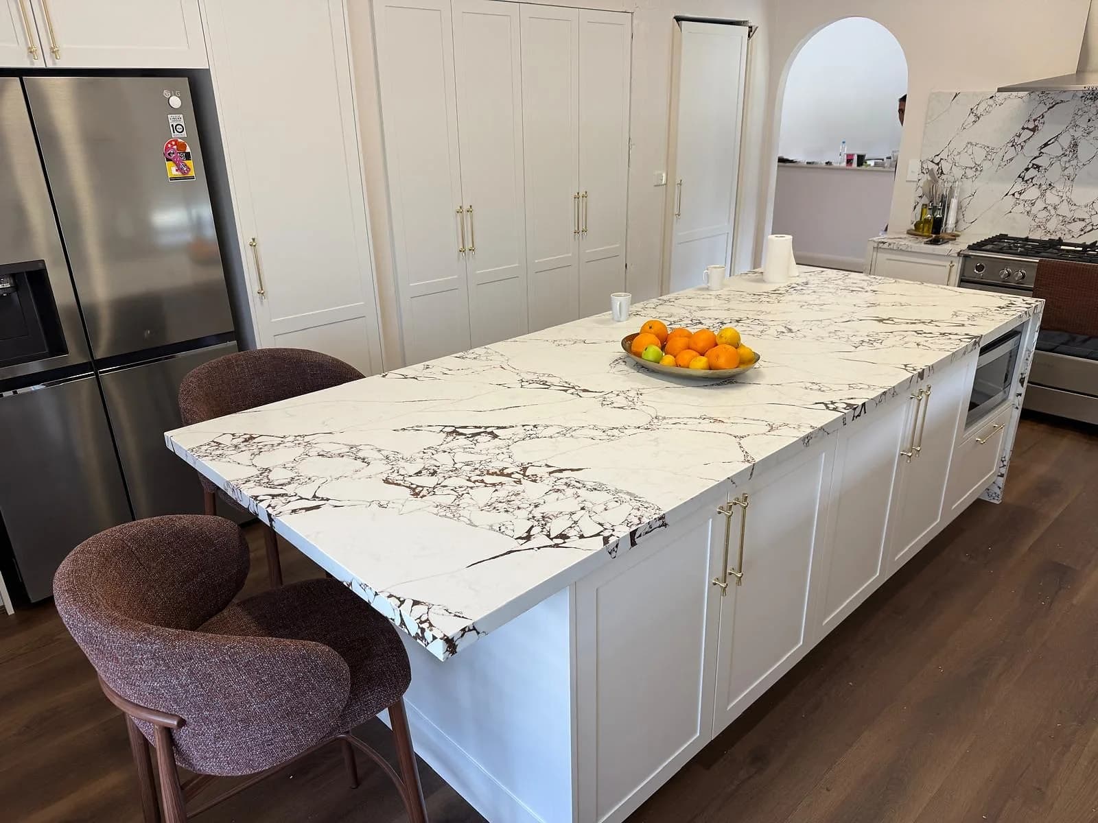 White shaker island with a bold marble-look benchtop and timber flooring by H&R Kitchens
